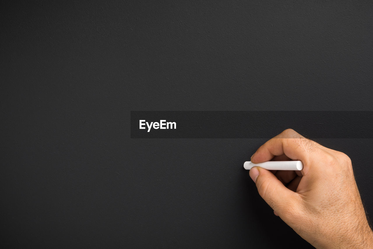 Close up of man hand holding chalk against blank black chalkboard