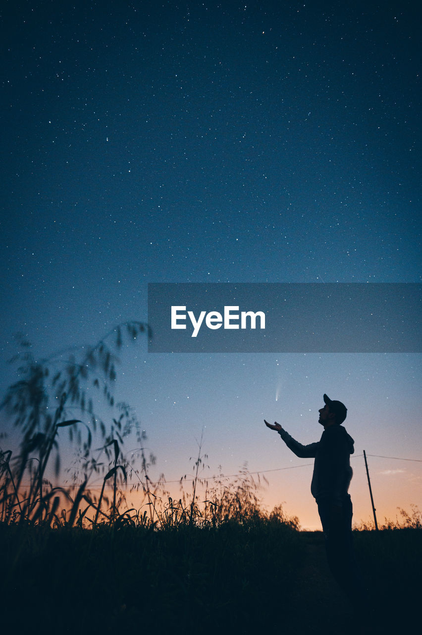 Silhouette man standing on field against sky at night catching a shooting star