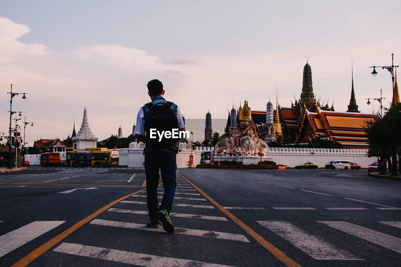 Rear view full length of man walking by temple on road in city