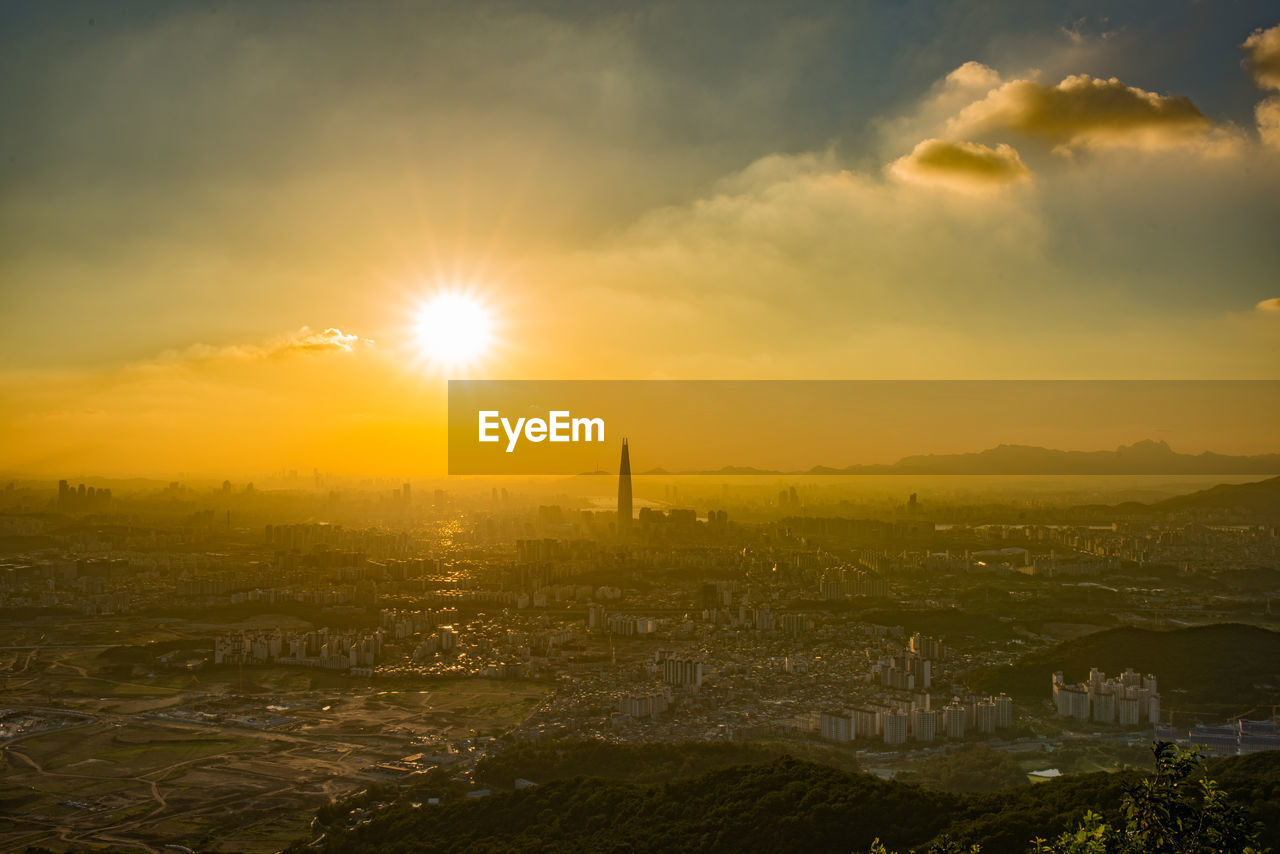 Aerial view of cityscape against bright sun in orange sky during sunrise