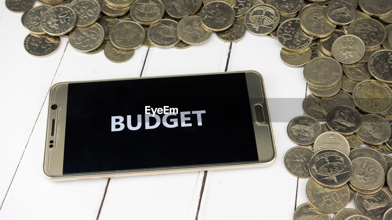 High angle view of budget text in smart phone by coins on table