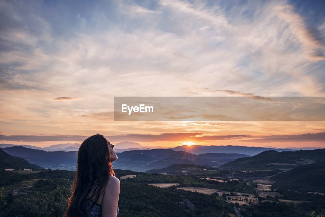 Young woman standing on mountain against sky during sunset