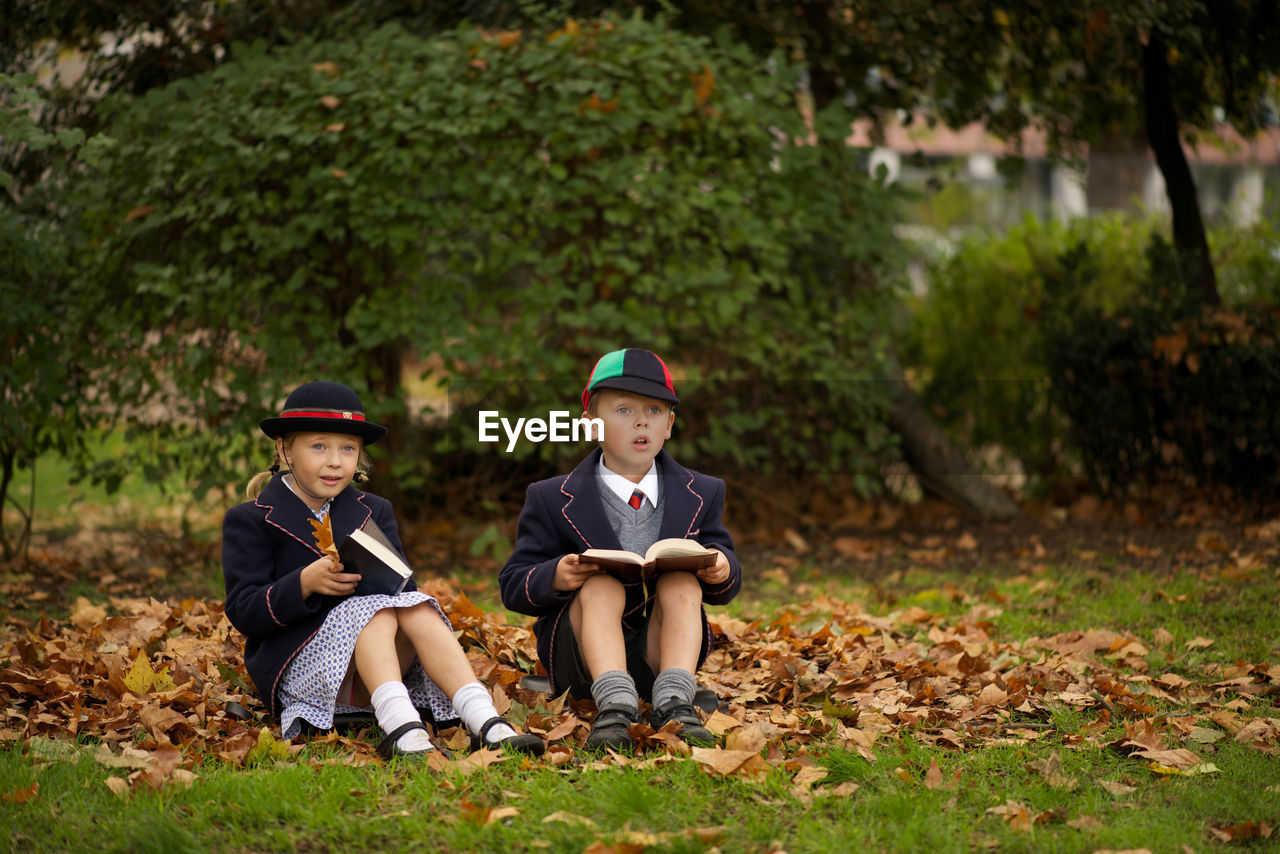 Full length of boy and girl reading books while sitting on grass