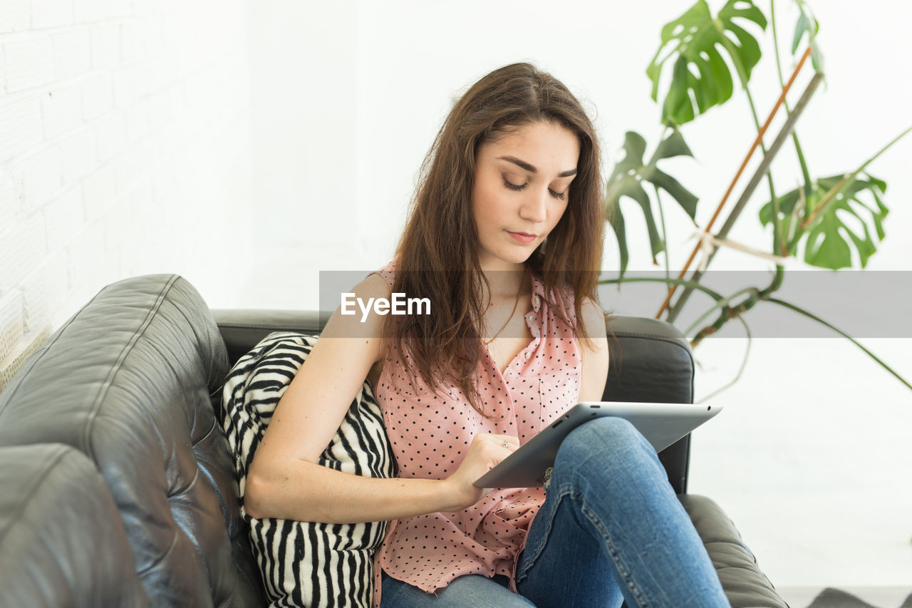 YOUNG WOMAN LOOKING AT CAMERA WHILE SITTING ON TABLE AT HOME