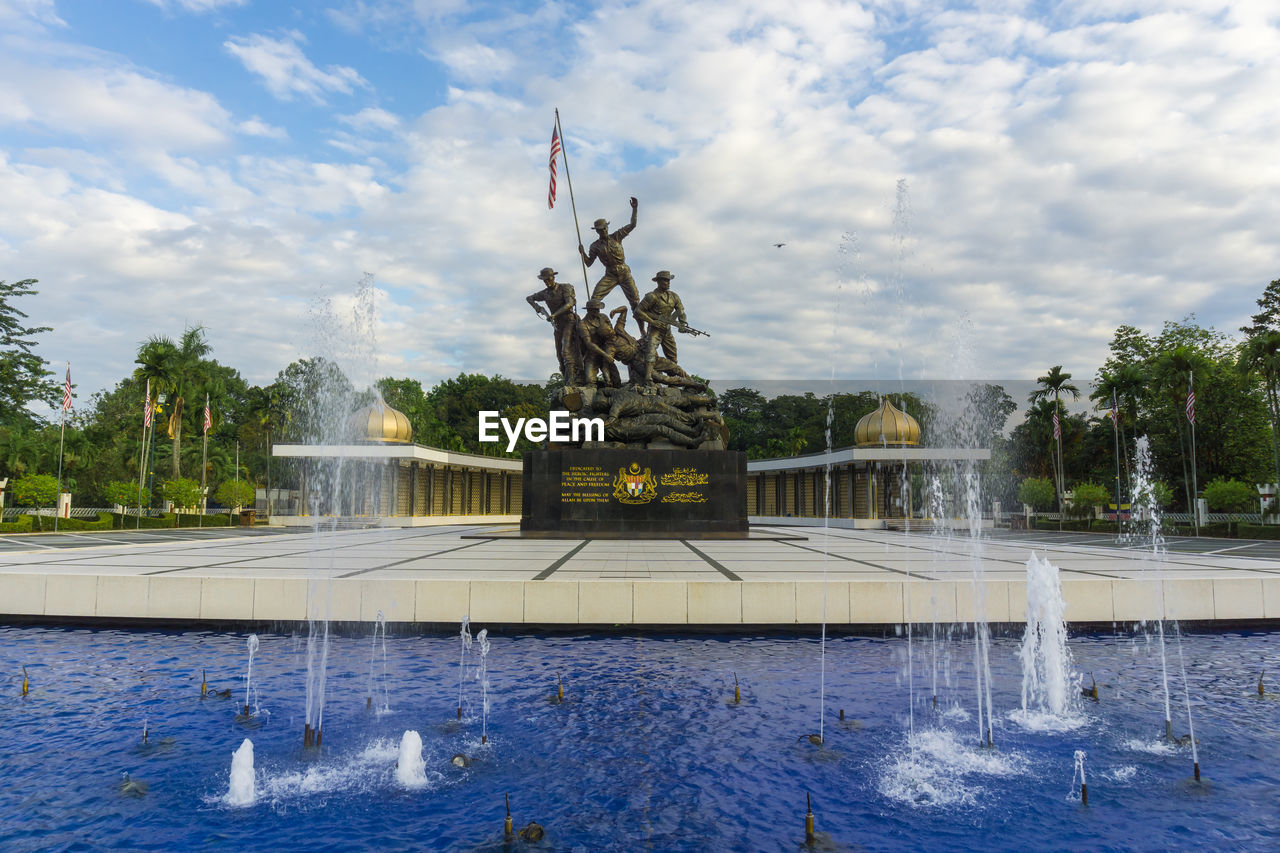 Statues amidst fountain against sky