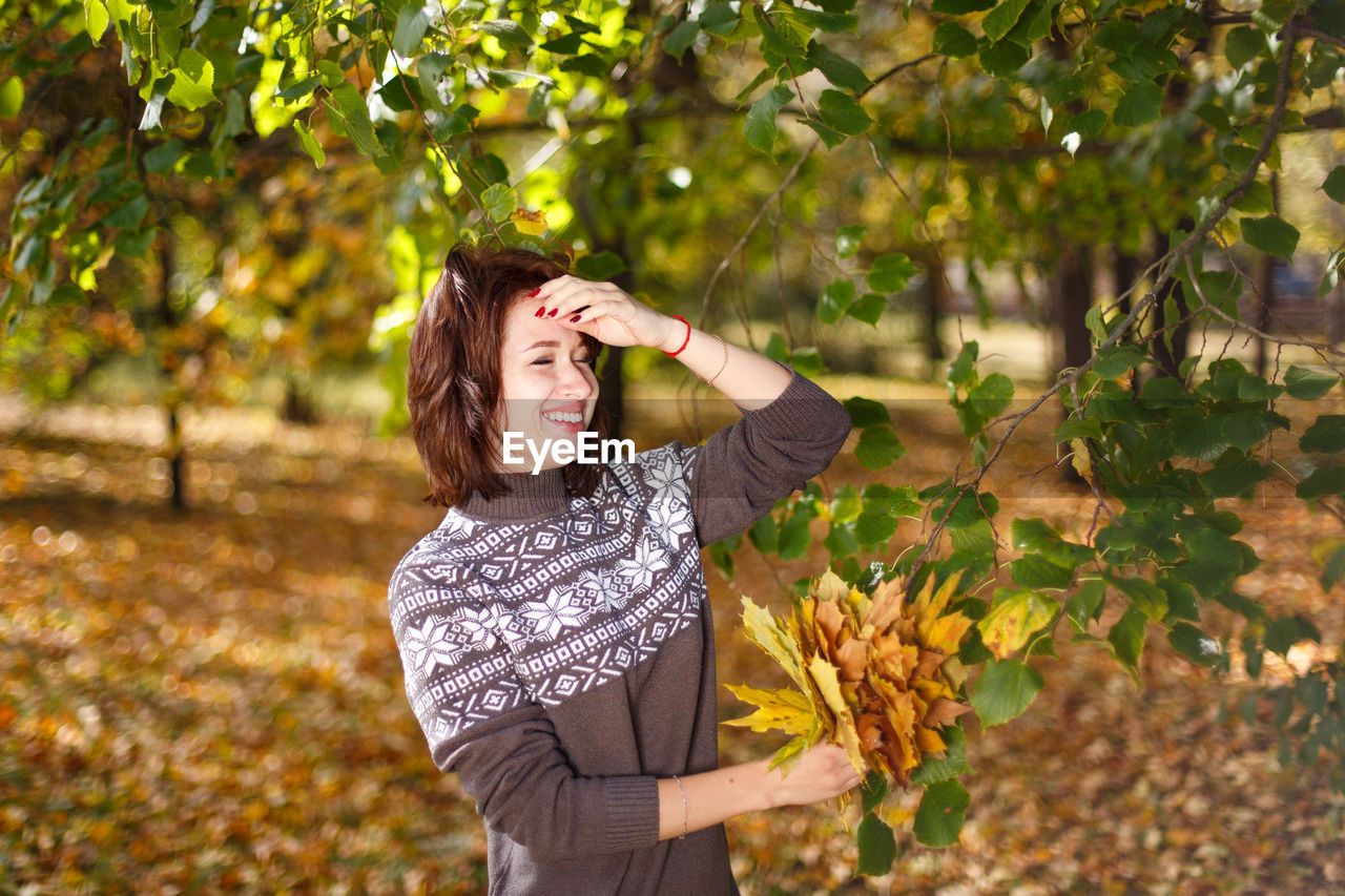 Happy caucasian young woman in a sweater holds bright autumn colors in her hand