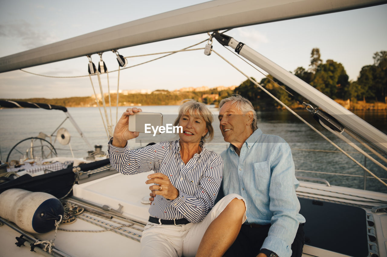 Smiling senior couple taking selfie on smart phone while sitting in boat