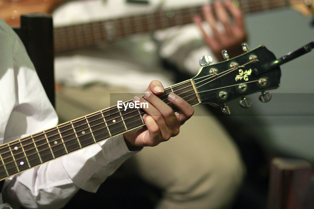 MIDSECTION OF MAN PLAYING GUITAR AT CAMERA