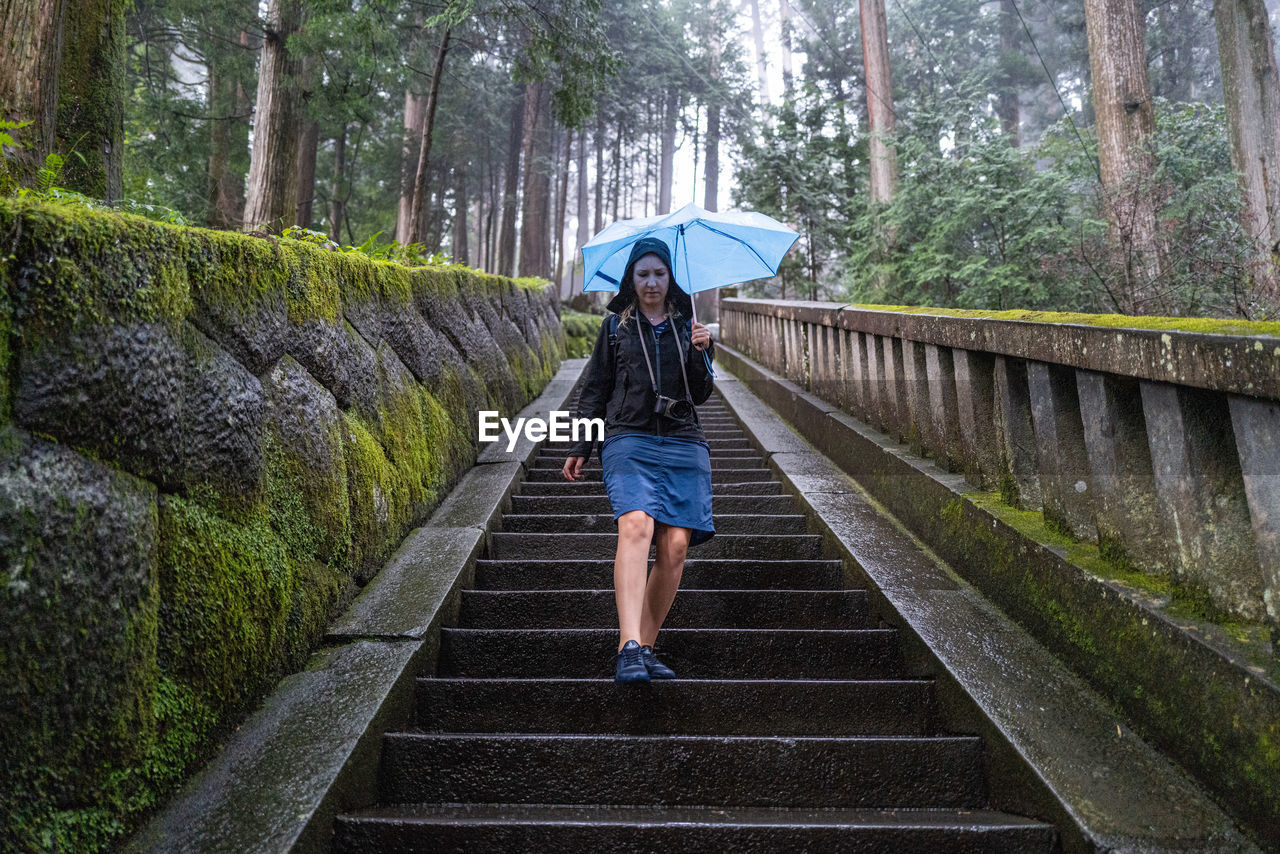 WOMAN WALKING ON WET FOOTBRIDGE IN FOREST