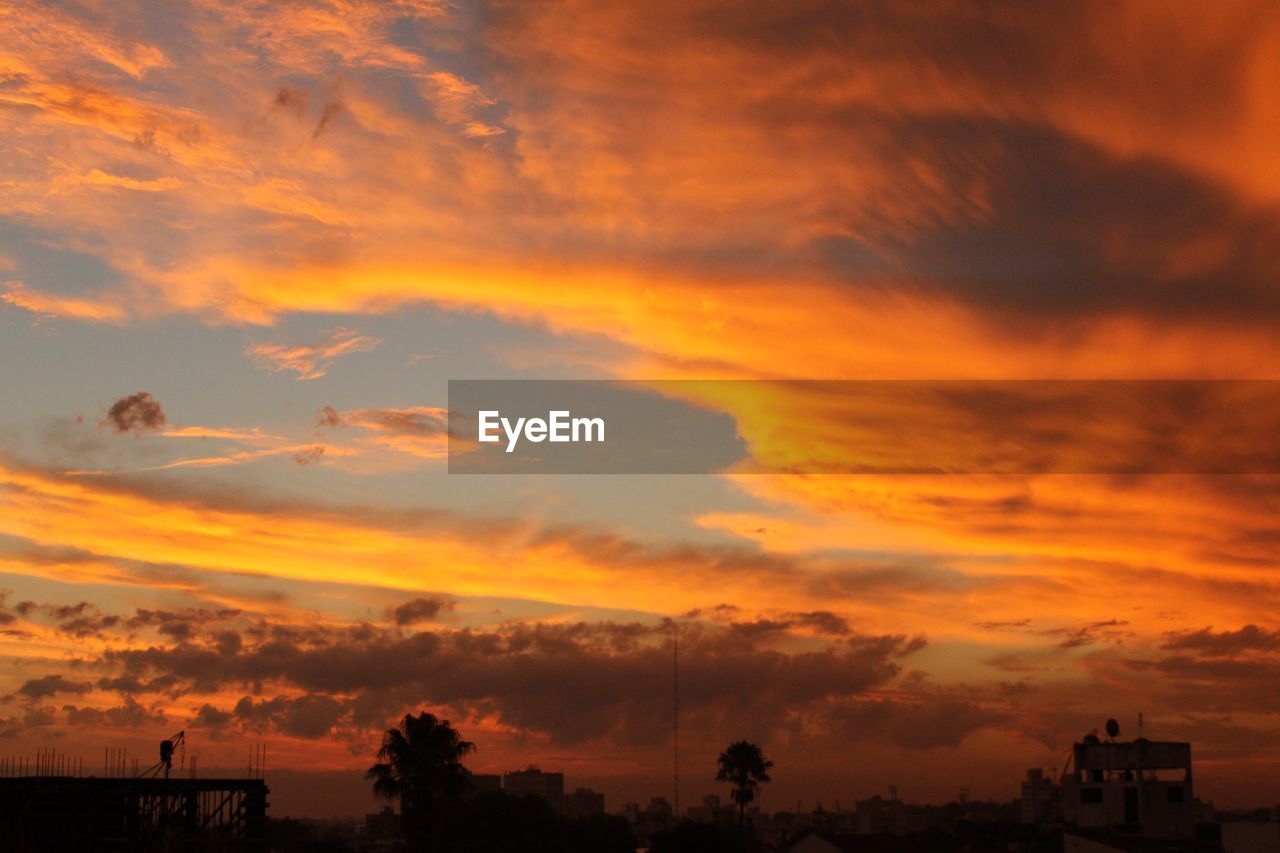 Silhouette buildings against orange cloudy sky