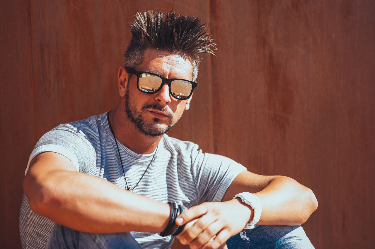 Portrait of handsome man wearing sunglasses while sitting against wall