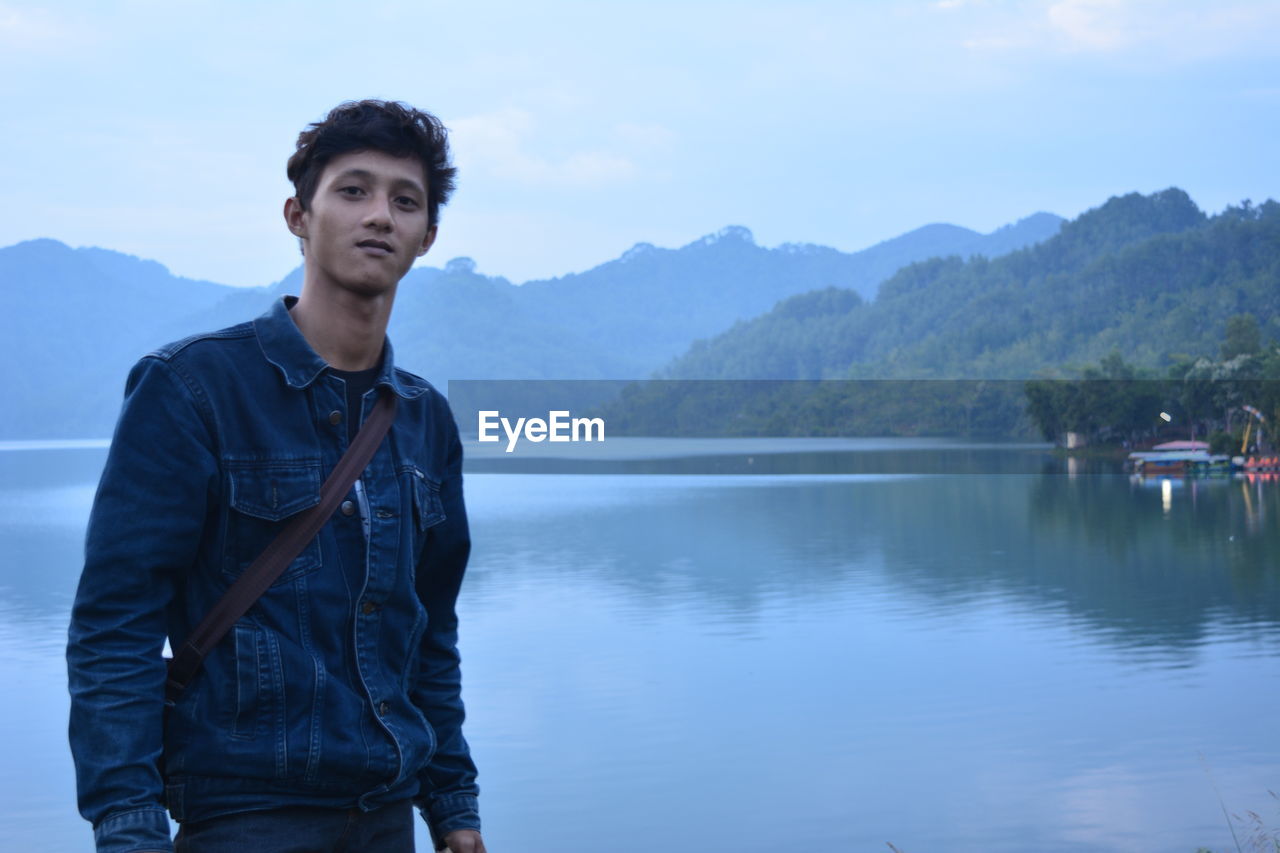 Young man standing by lake against mountains