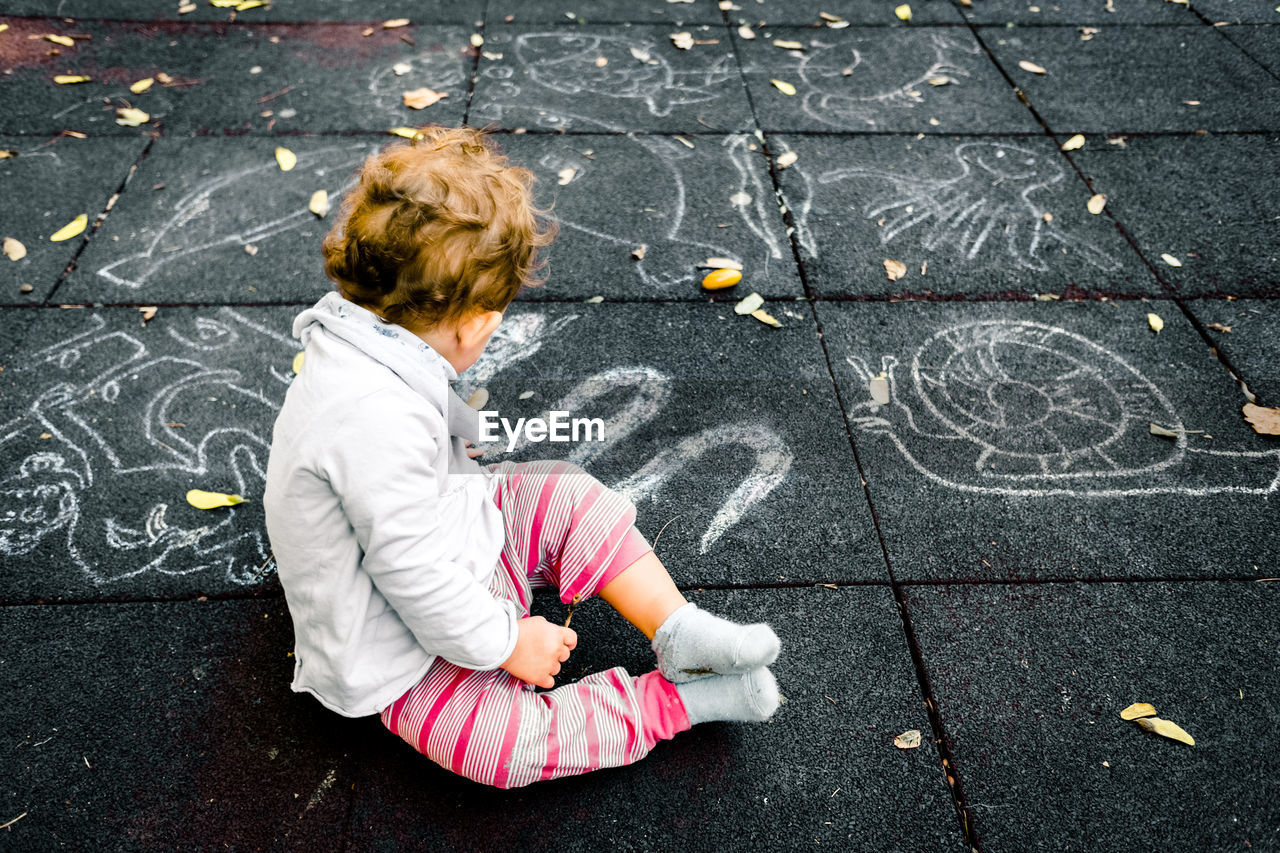 HIGH ANGLE VIEW OF CHILD SITTING ON FOOTPATH