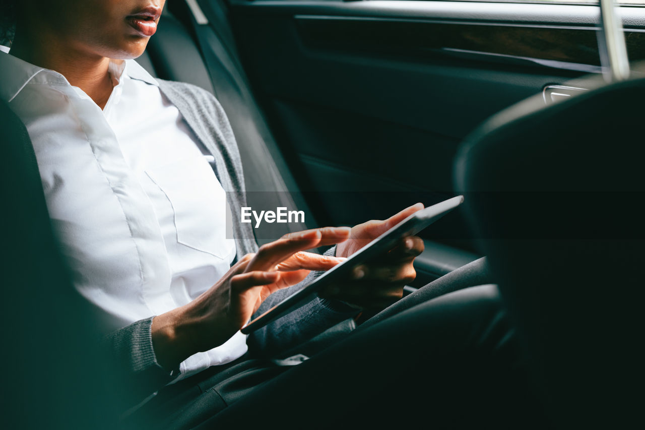 Midsection of woman using tablet while sitting in car