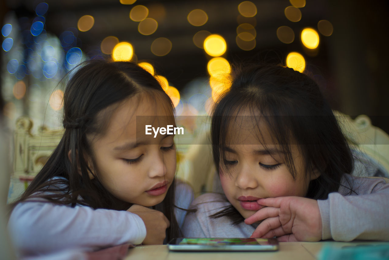 Sisters playing game on mobile phone at home during night