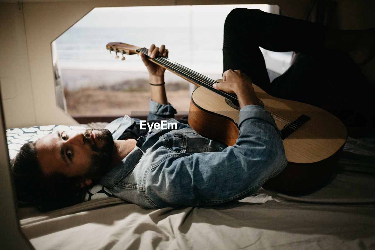 Man playing guitar while lying down on bed