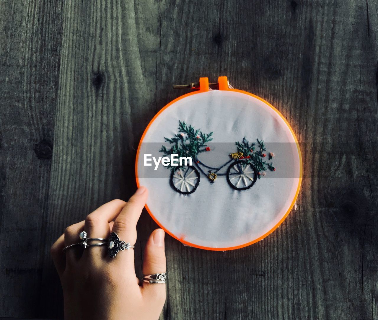Cropped hand holding embroidery ring with bicycle design on fabric