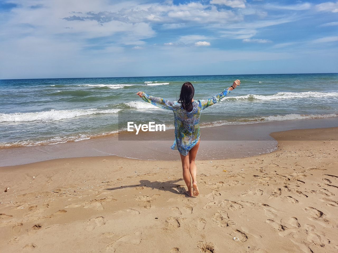 Full length rear view of woman with arms outstretched walking at beach