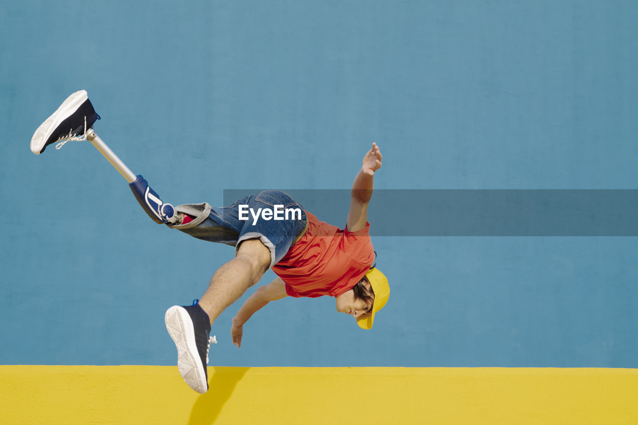 Man with artificial limb and foot jumping against multi colored wall