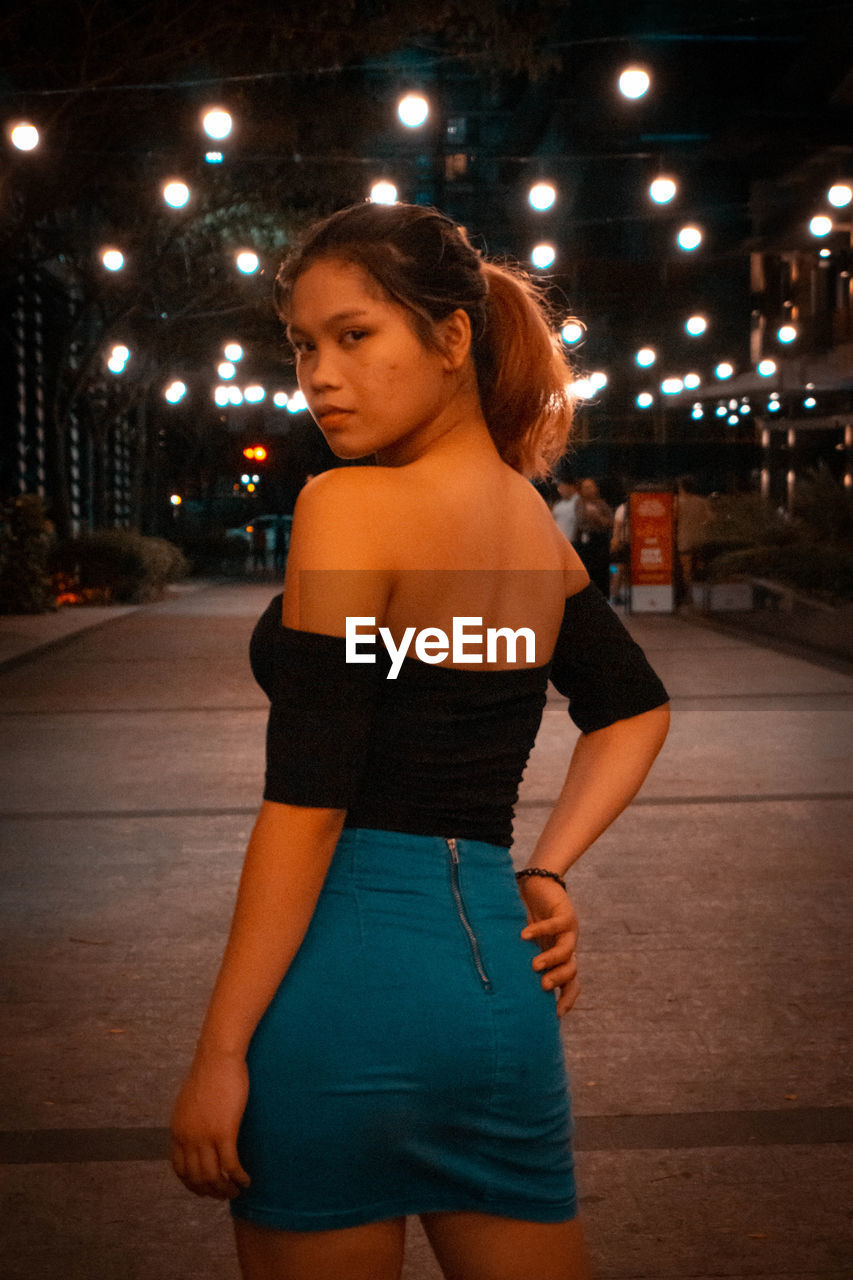 YOUNG WOMAN STANDING ON STREET AT NIGHT