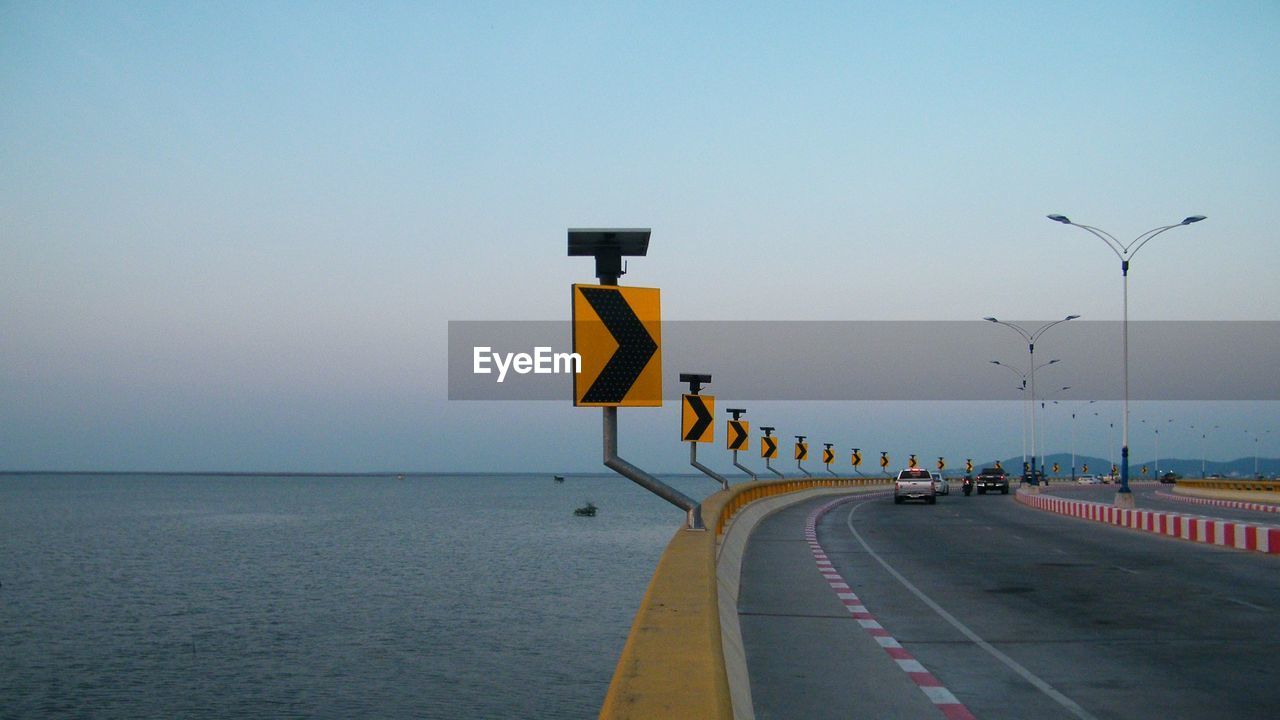 Road sign on street by sea against clear sky