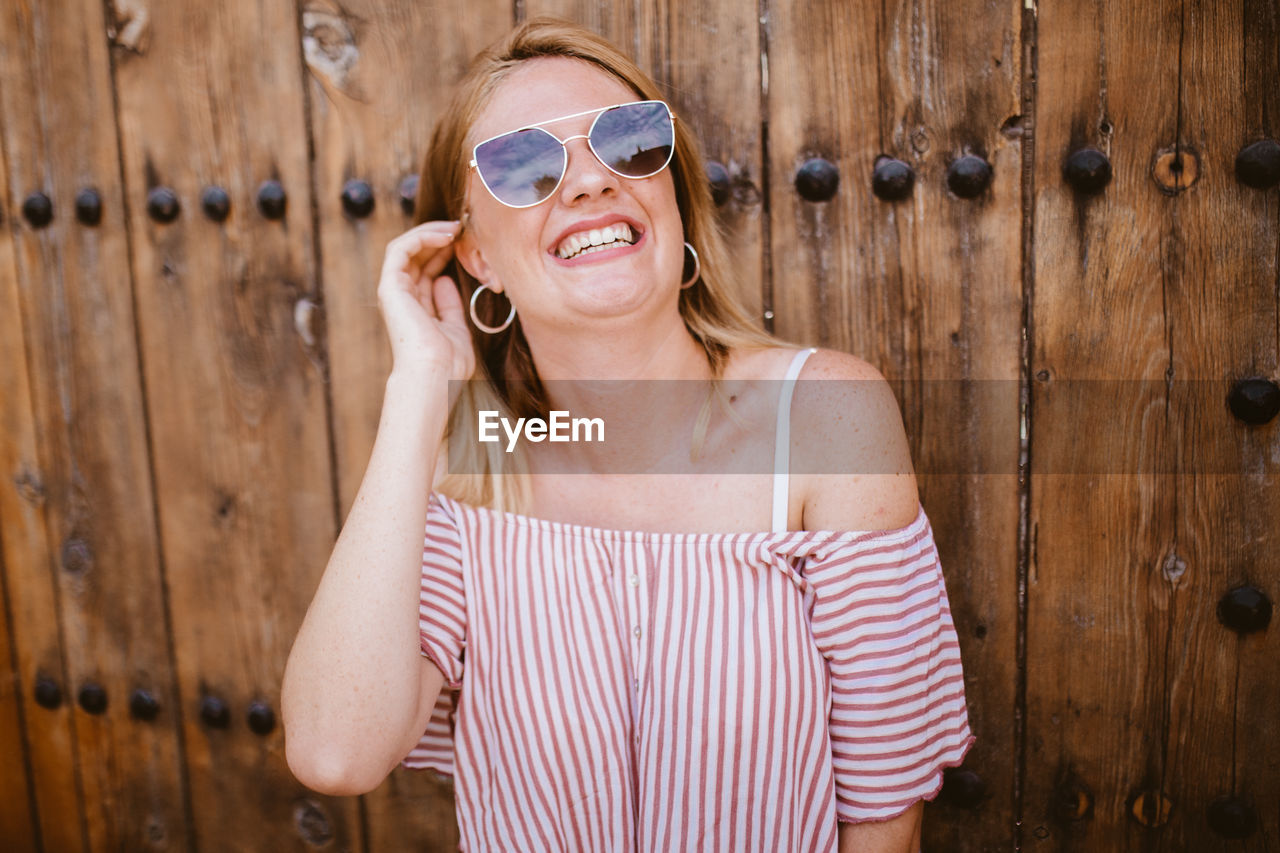 Blonde woman with sunglasses laughing and touching her hair