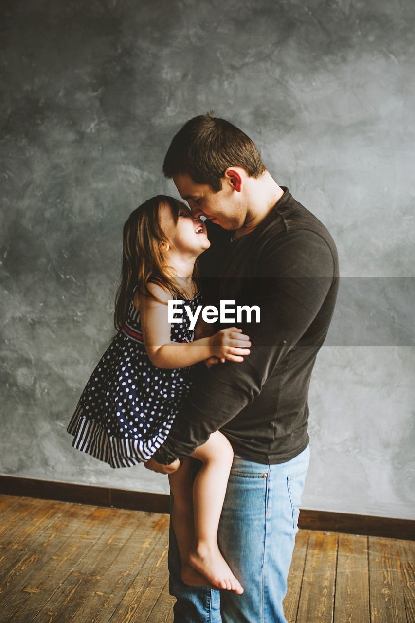 Side view of happy father holding girl while standing on hardwood floor