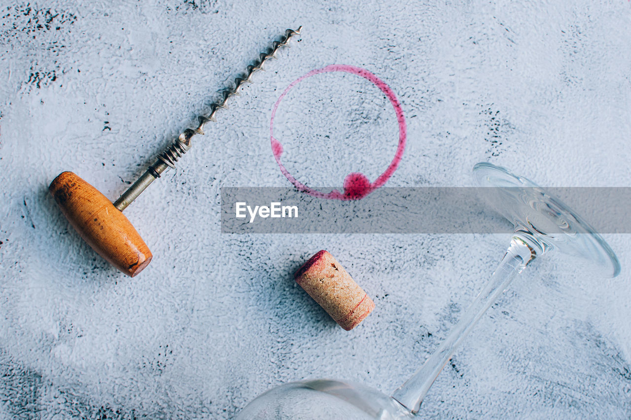 Top view of vintage corkscrew, cork, wineglass and red wine stain or ring over gray background