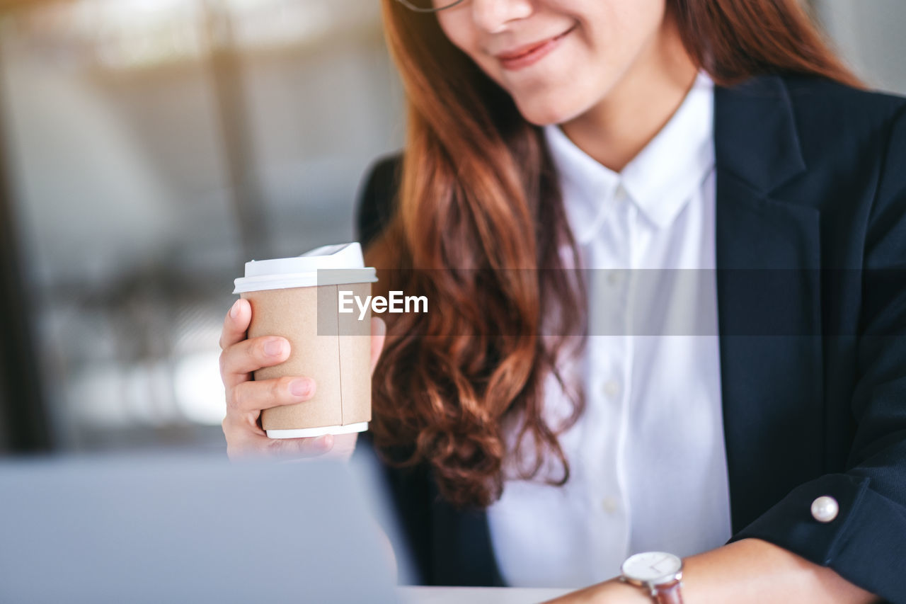 Midsection of woman drinking coffee while using sitting by desk in office