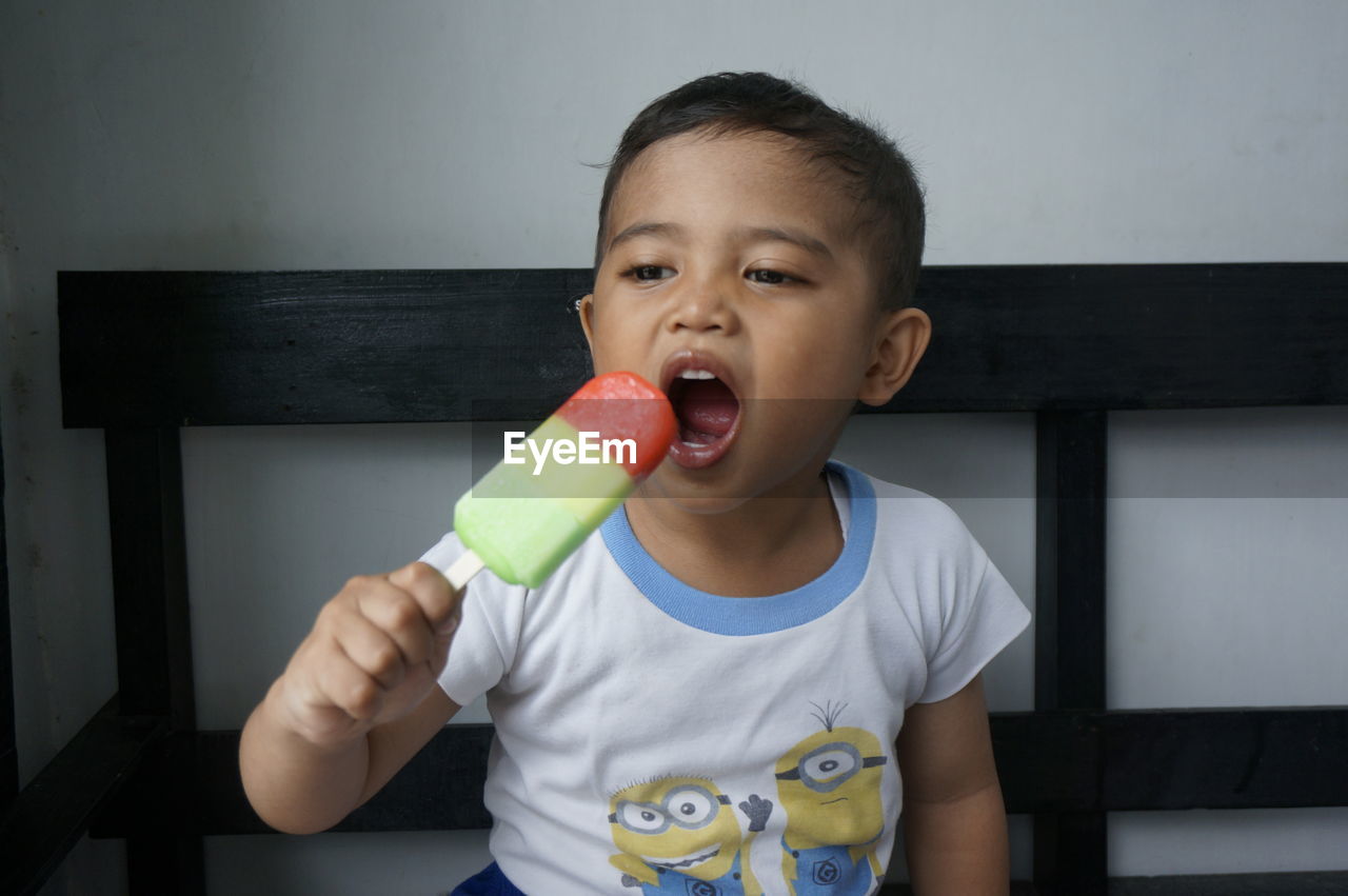 Boy eating flavored ice while sitting on bench