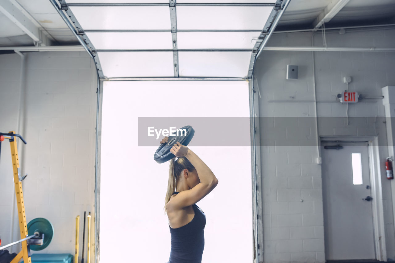 Woman lifting weight plate while exercising in gym