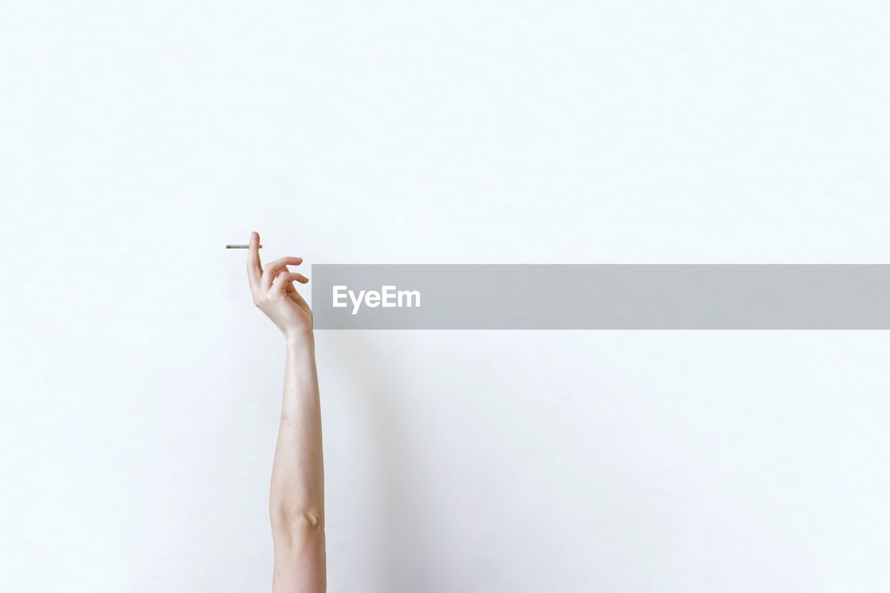 Cropped hand holding cigarette against white background