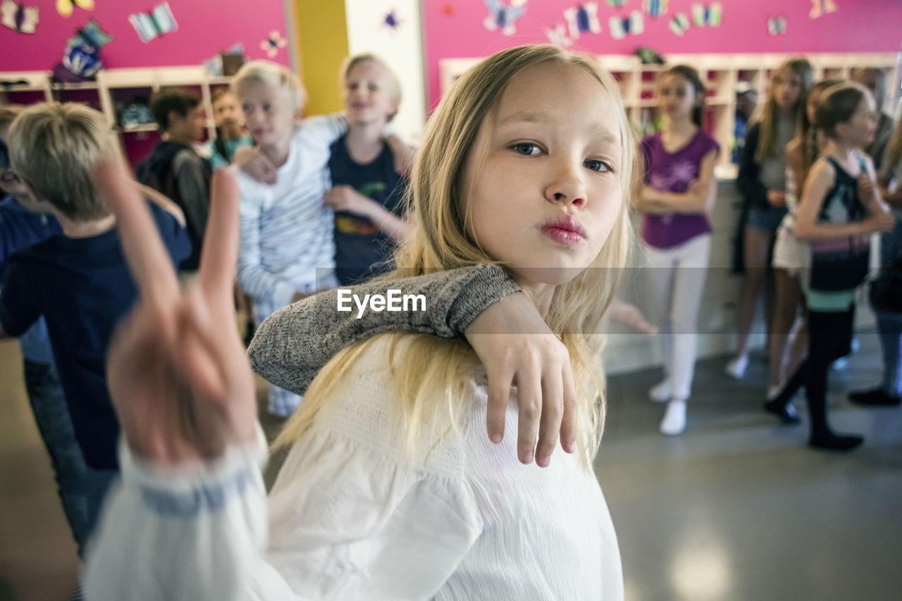 Schoolgirl showing peace sign with friends in corridor