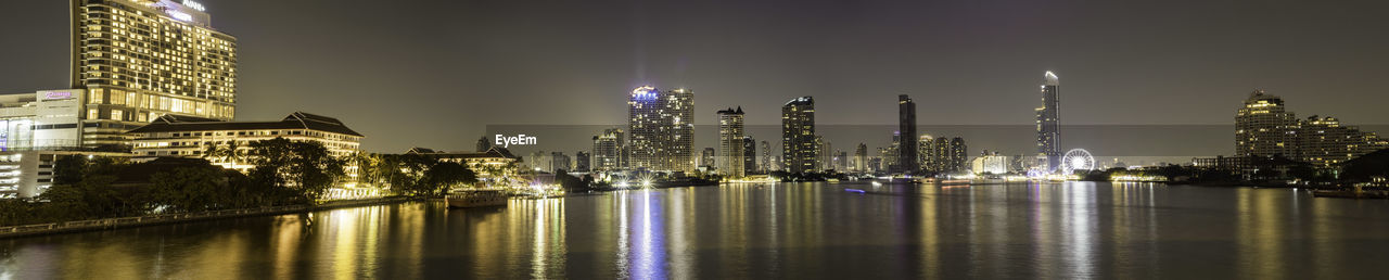 ILLUMINATED BUILDINGS BY RIVER AGAINST SKY