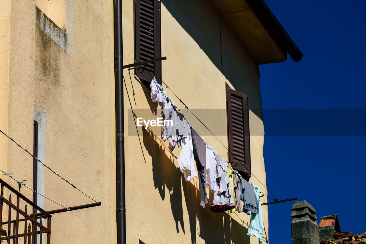 Low angle view of laundry drying on clothesline of residential building against clear blue sky