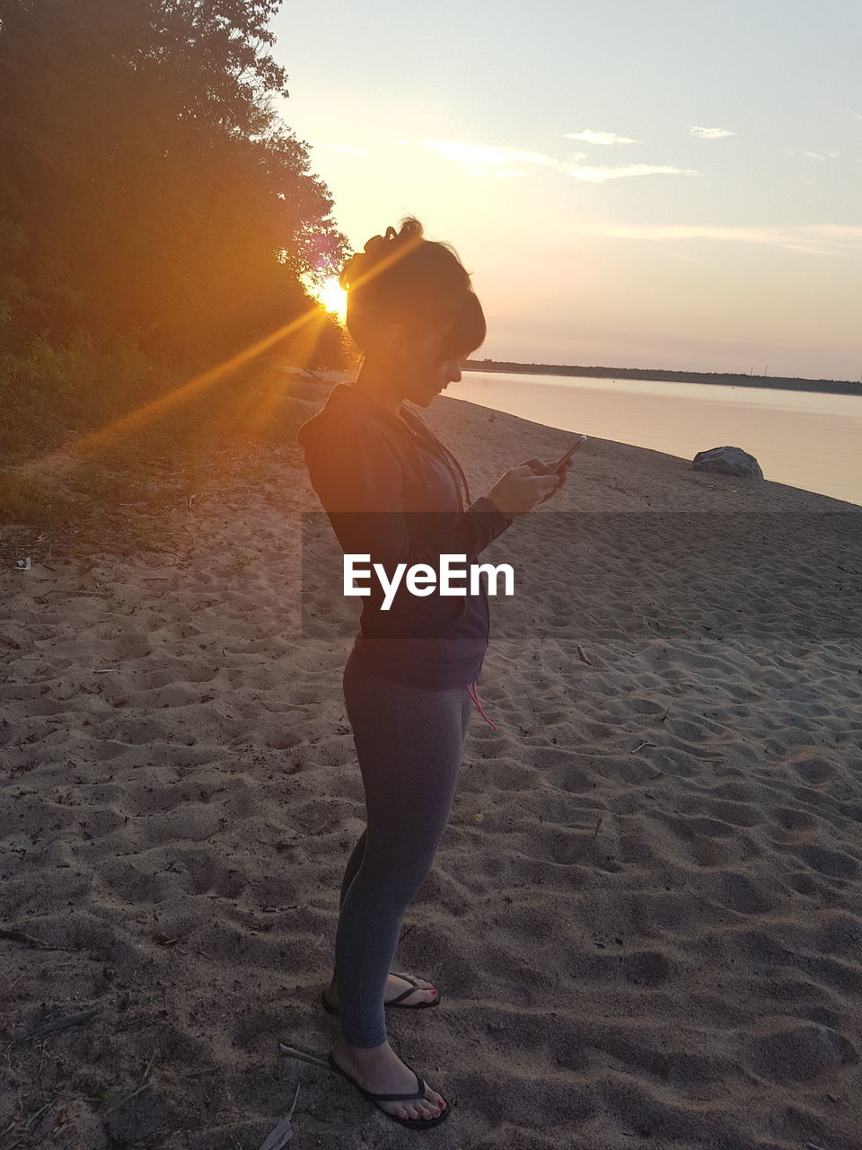 BOY STANDING ON BEACH AGAINST SUNSET SKY