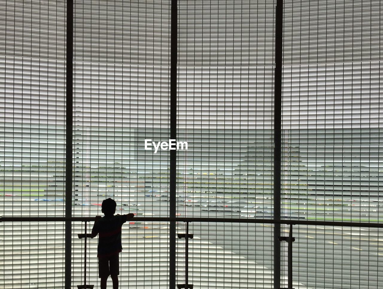 Silhouette rear view of boy looking through window