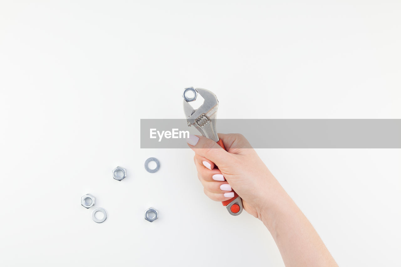 Close-up of hand holding wrench by nuts over white background