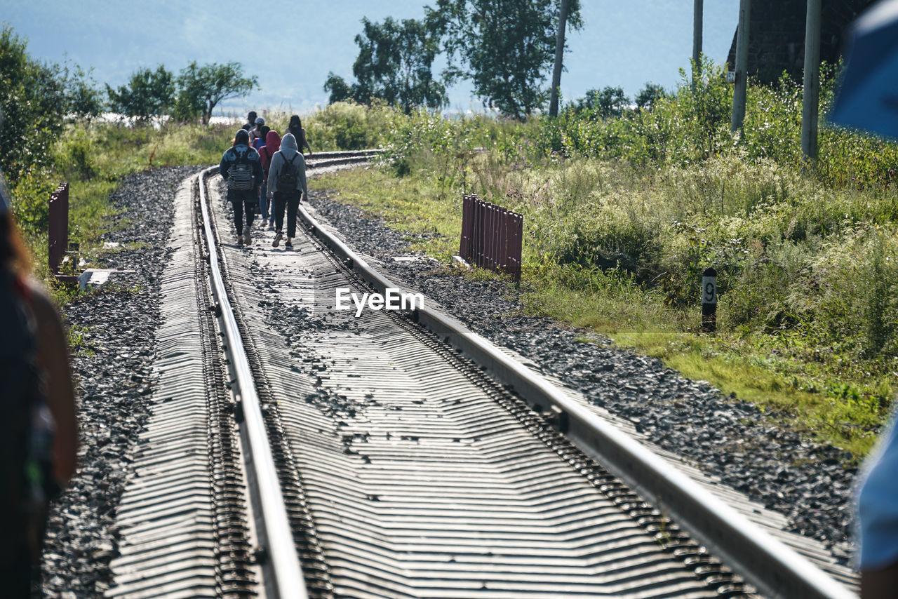 REAR VIEW OF PEOPLE WALKING ON RAILROAD TRACKS BY TREES