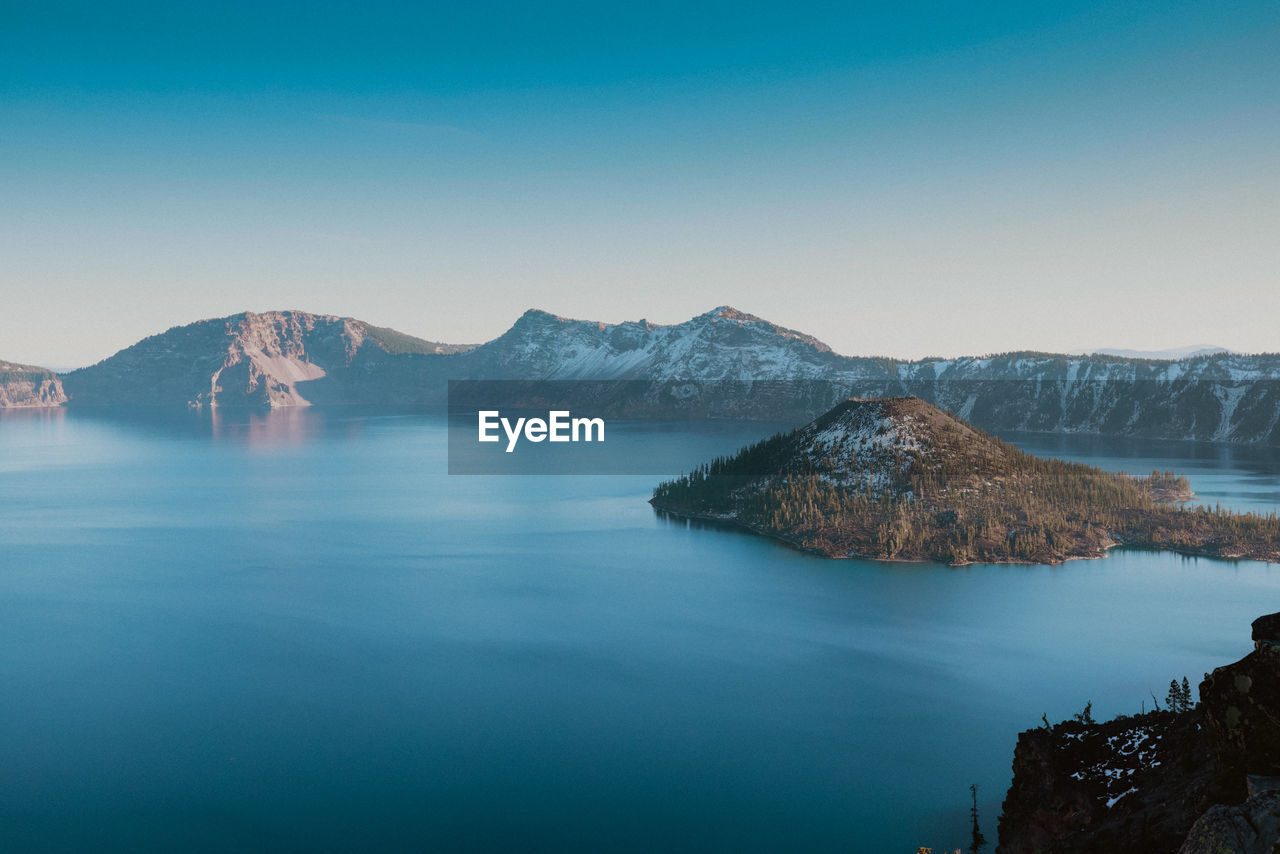 Scenic view of sea and mountains against clear blue sky