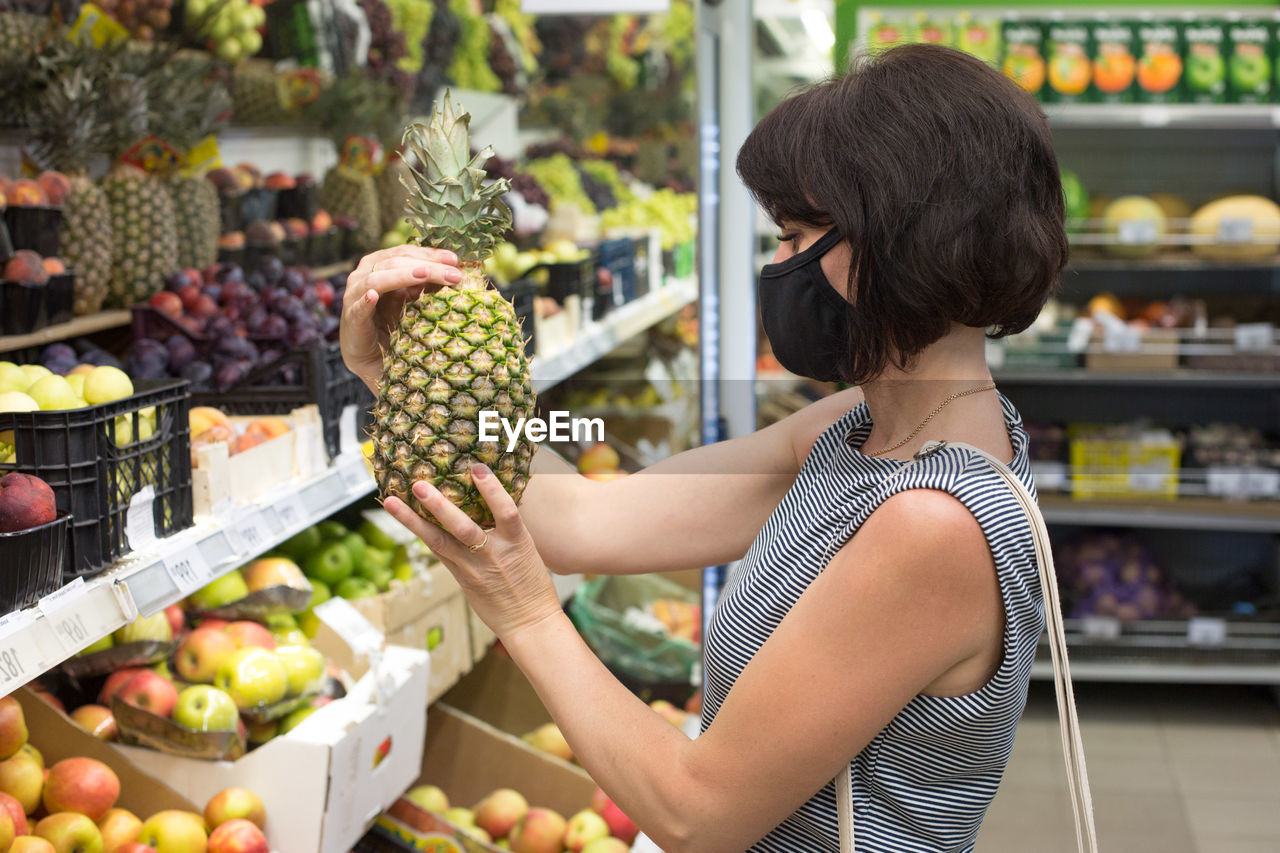 Woman buyer in a protective medical mask chooses a pineapple store. person