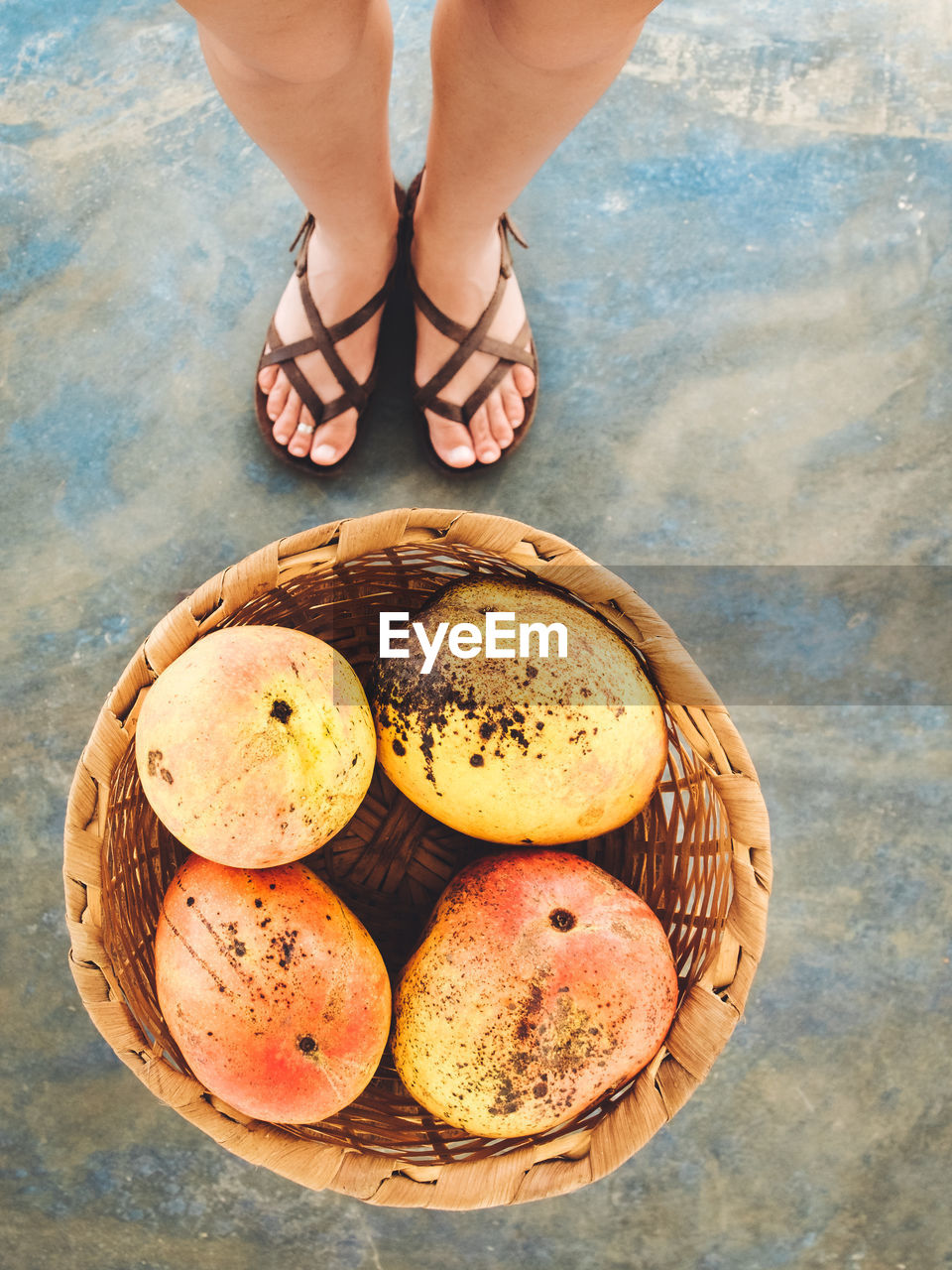 Low section of woman standing on mangoes in wicker basket at beach