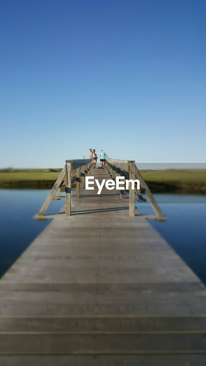 Distant view of people on footbridge over lake against clear sky