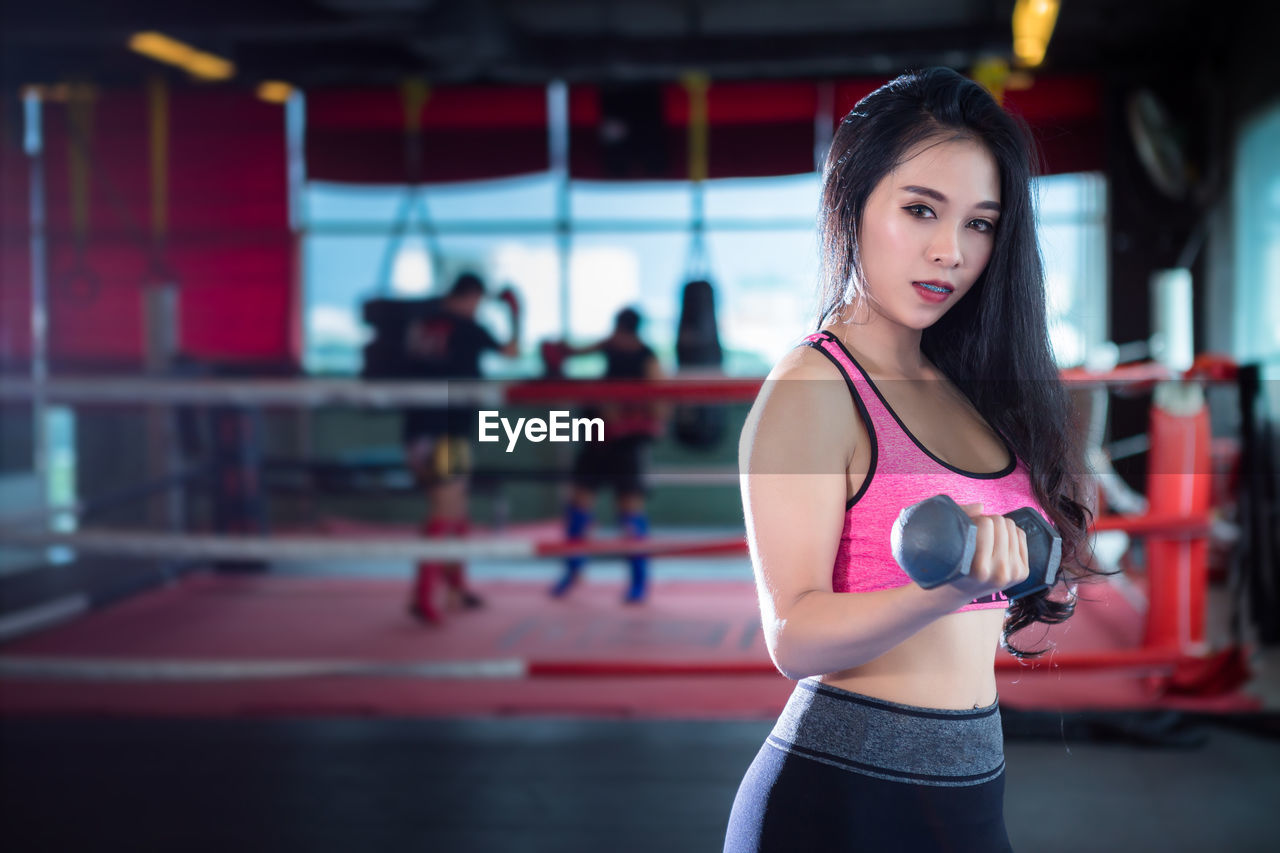 Confident young woman holding dumbbell while exercising in gym