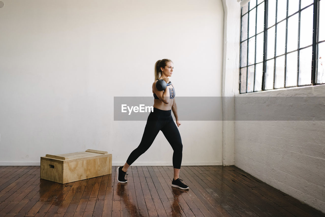 Female athlete carrying kettlebell while standing in gym