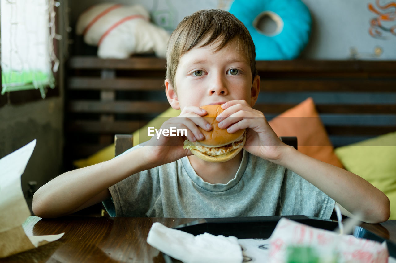 Boy eating a big burger with a cutlet. hamburger in the hands of a child. delicious chicken burger.