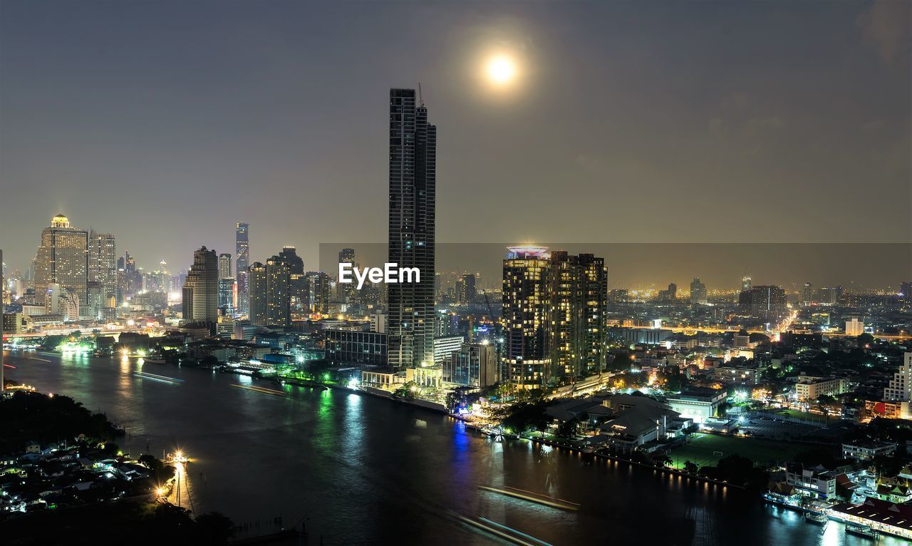 Illuminated buildings by river against sky in city at night