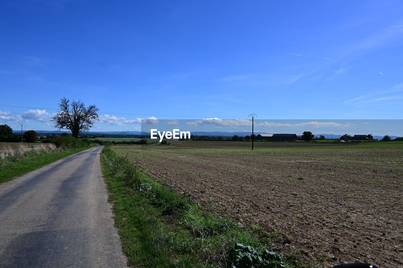 sky, horizon, landscape, environment, road, field, transportation, rural area, nature, plant, land, rural scene, blue, cloud, scenics - nature, agriculture, the way forward, plain, no people, hill, grass, diminishing perspective, beauty in nature, infrastructure, dirt, tranquility, soil, vanishing point, highway, tranquil scene, non-urban scene, prairie, dirt road, outdoors, day, farm, tree, travel, country road, street, empty road