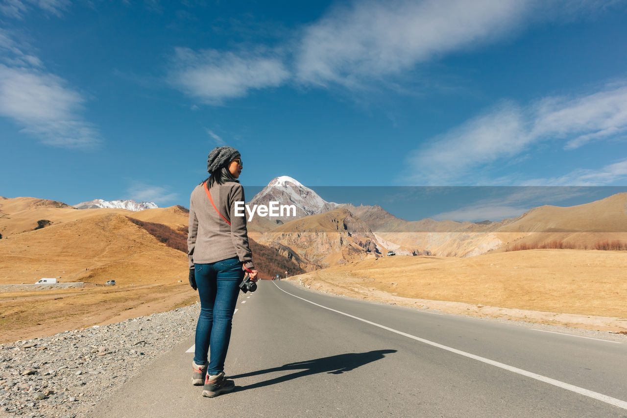 Woman standing on road by mountains against sky