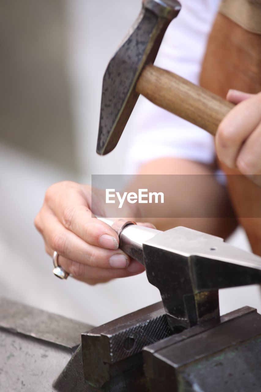 Midsection of person hammering metal in workshop